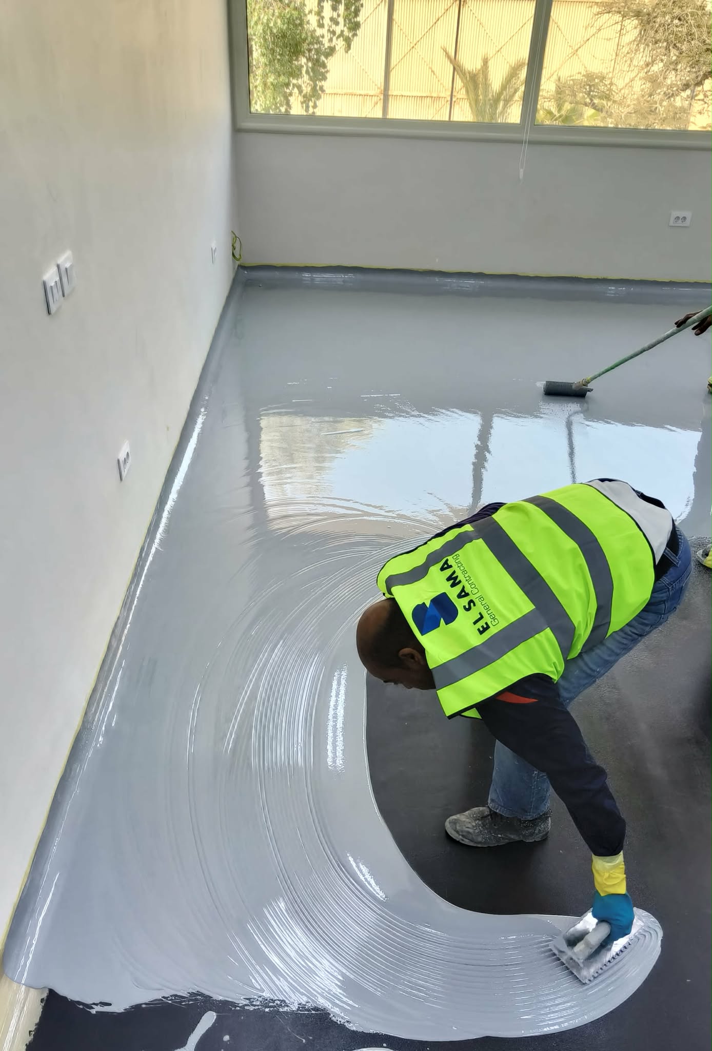 Applicator troweling self-leveling epoxy across a room floor